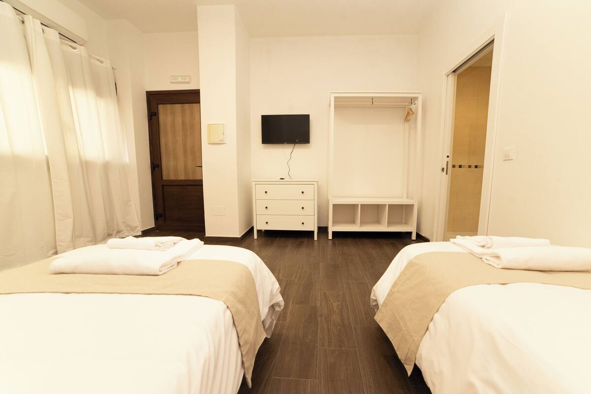 A hotel room with two beds, a TV, a wardrobe, and a bench.