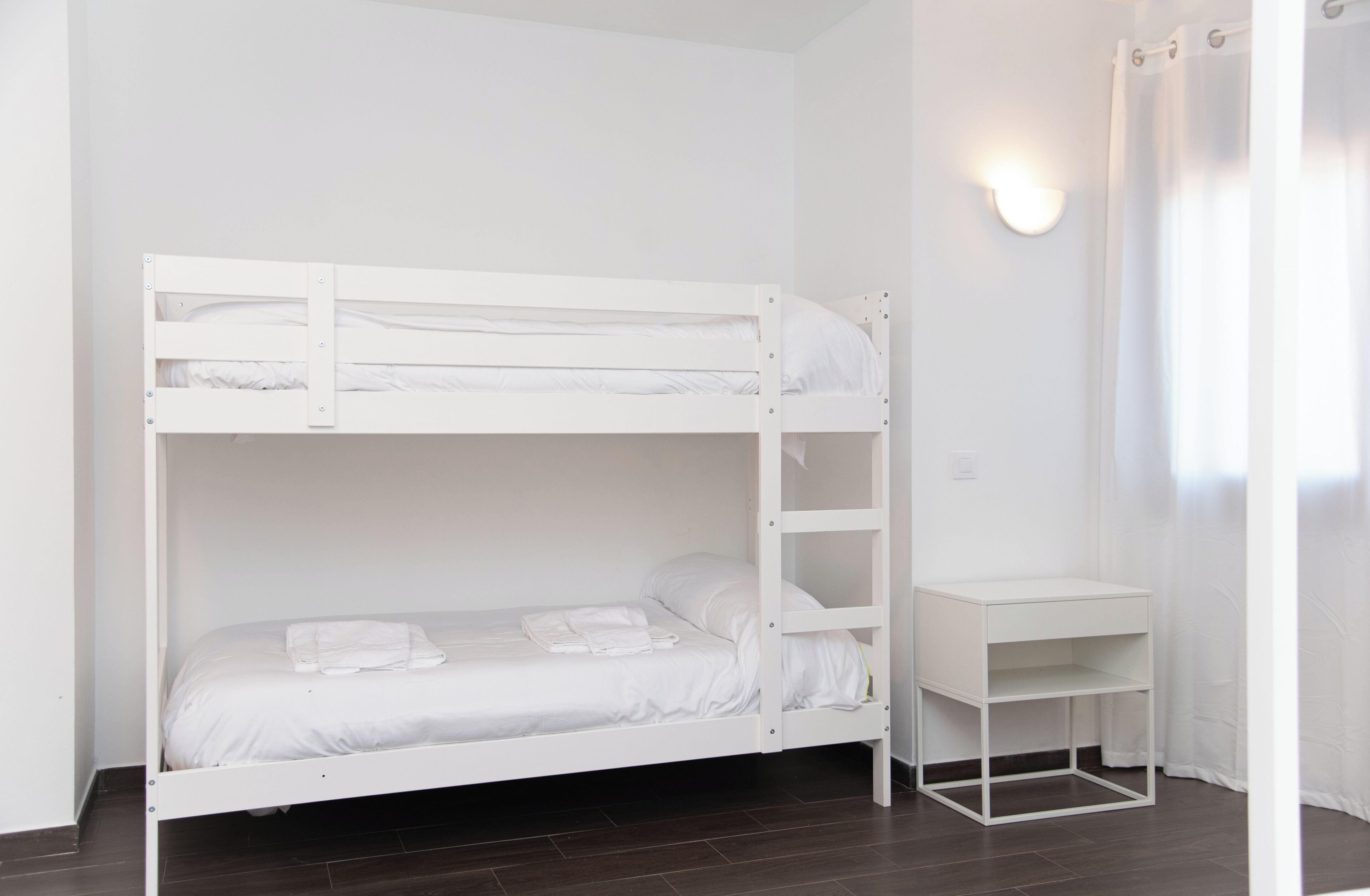 Una cama litera con escritorio y estantería en una habitación con paredes blancas y suelo oscuro.