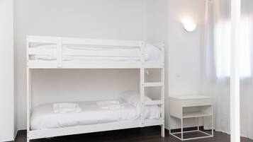 Una cama litera con escritorio y estantería en una habitación con paredes blancas y suelo oscuro.