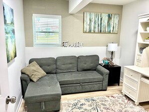 A living room with a grey sofa, a small side table with a lamp, a white dresser, and two abstract paintings on the wall. - Charming Private Suite with Game Room in Athens (Athens)