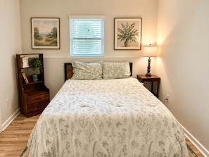 A bedroom with a bed, a nightstand, a lamp, a window with blinds, and two framed pictures on the wall. - Charming Private Suite with Game Room in Athens (Athens)