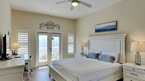A bedroom with a bed, bedside tables, a ceiling fan, and a view through the door. - Pavilion Palms #201A | Central Location + Close to Beach! (Miramar Beach)