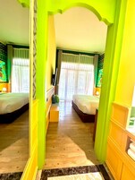 Ein Zimmer mit zwei Betten, Holzboden, einem grünen Bogen und einem Fenster mit Vorhängen.