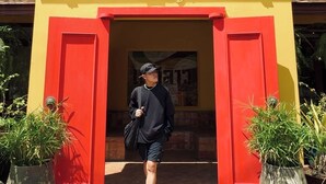 Ein Gebäudeeingang mit gelber Fassade und roten Türen, mit einem Schild mit thailändischen Schriftzeichen.