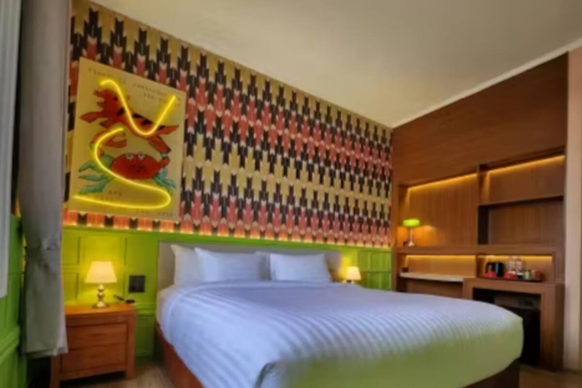 Una habitación de hotel con una cama grande, dos mesitas de noche con lámparas, un papel tapiz estampado y un cabecero de madera.