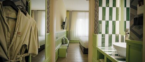Un pasillo estrecho con una cama, un baño con salpicadero de azulejos blancos y verdes a cuadros, y un perchero.