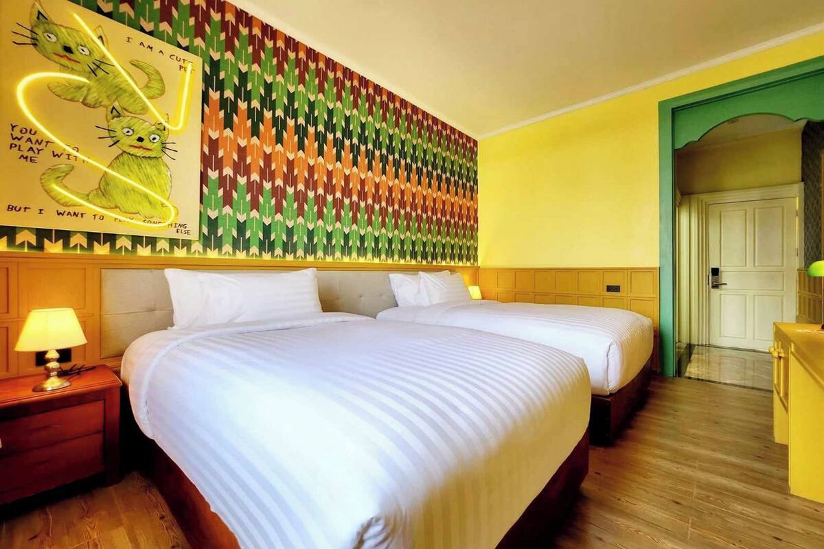 Habitación de hotel con dos camas, suelo de madera, pared con diseño y una puerta a la derecha.