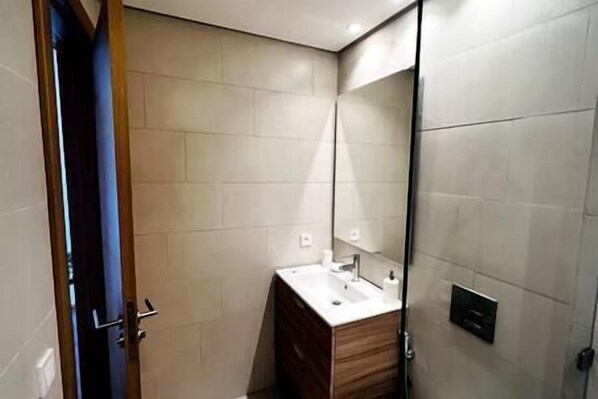 Un baño moderno con tocador de madera, un espejo grande y un aplique de pared.