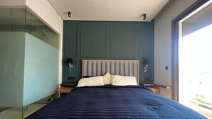 A modern bedroom with a large bed, a headboard, bedside tables, and a glass partition.