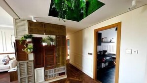 A room with a wooden floor, a ceiling with a green leaf design, and a doorway leading to a kitchen area.