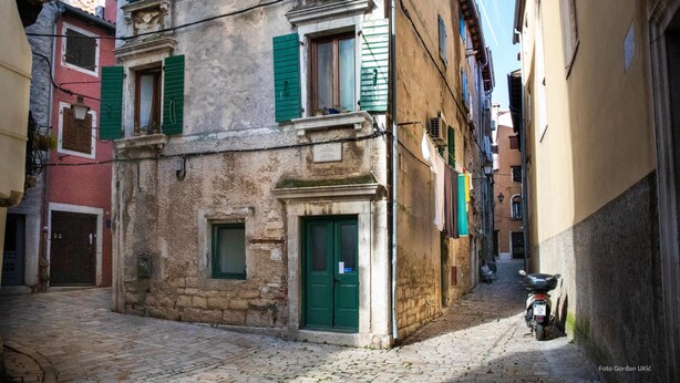 A narrow cobblestone street with historic buildings, a motorcycle parked on the right, and a green door on the left. - Studio Oratorio (Rovinj)