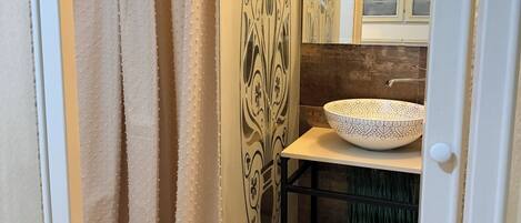 A bathroom with a shower curtain, a sink with a decorative bowl, and a mirror with a cabinet.