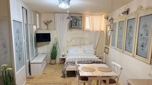 A bedroom with a bed, bedside table, TV, and a dining area with chairs and a table. - Studio Oratorio (Rovinj)