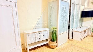 A room with a white cabinet, a white console table, a woven basket with a plant, and a television on a stand. - Studio Oratorio (Rovinj)