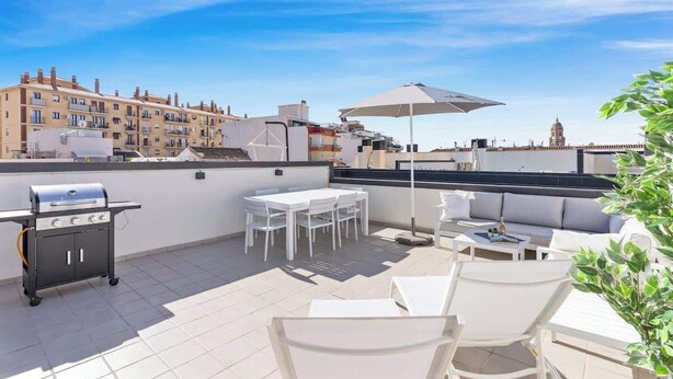Una terraza en la azotea con una parrilla, mobiliario blanco y vistas a edificios.