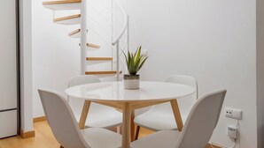 Una habitación moderna y minimalista con una escalera espiral blanca, una mesa redonda de madera y sillas blancas, y una planta en maceta.