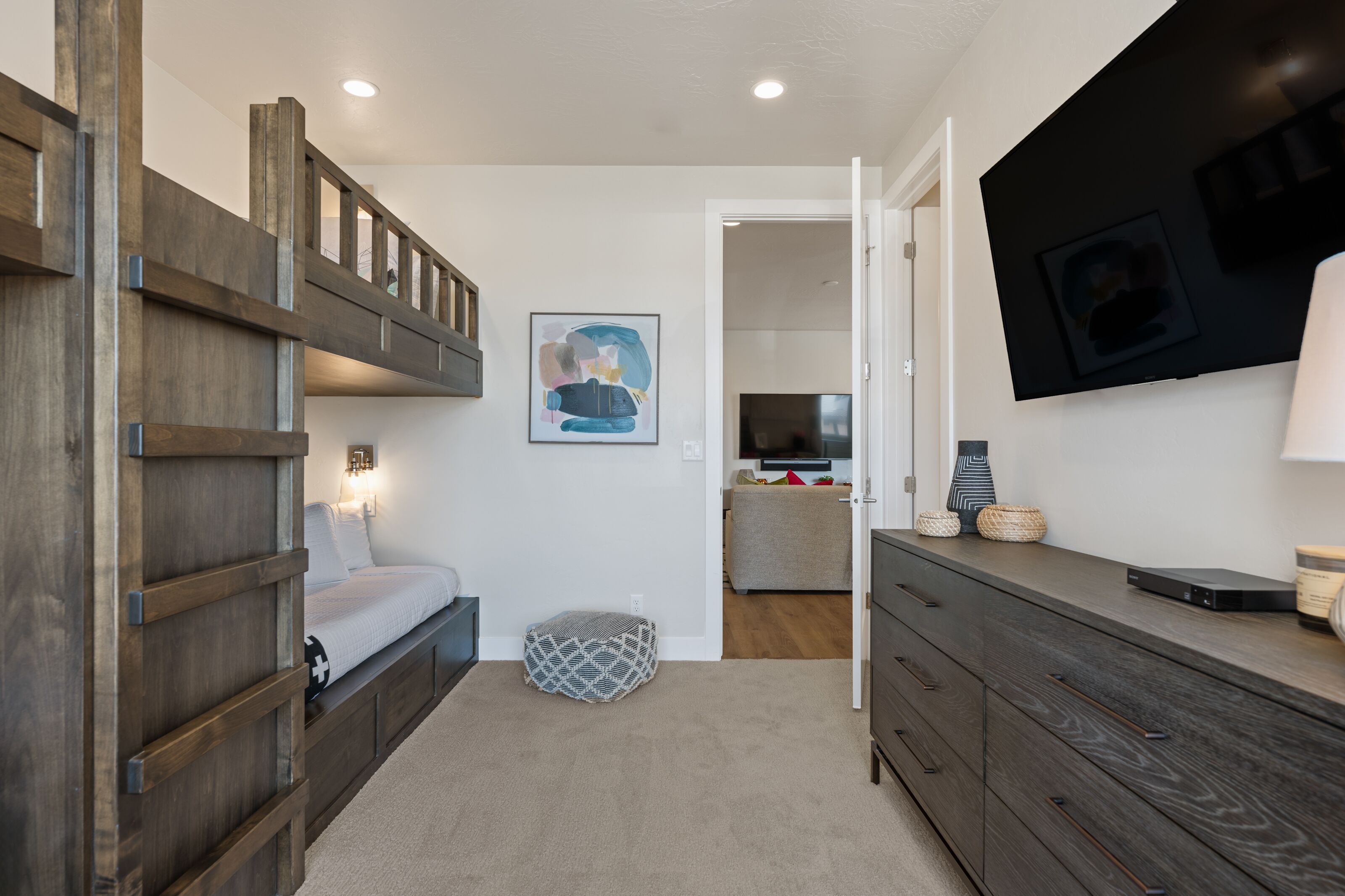 A bedroom with a bunk bed, a bedside table, a lamp, and a TV mounted on the wall.