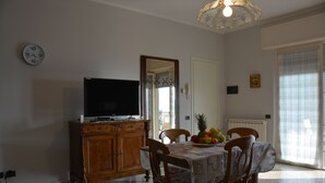 Una zona de menjador amb una taula preparada per a quatre, un moble de baderons amb televisió, i un plat de fruita sobre la taula.