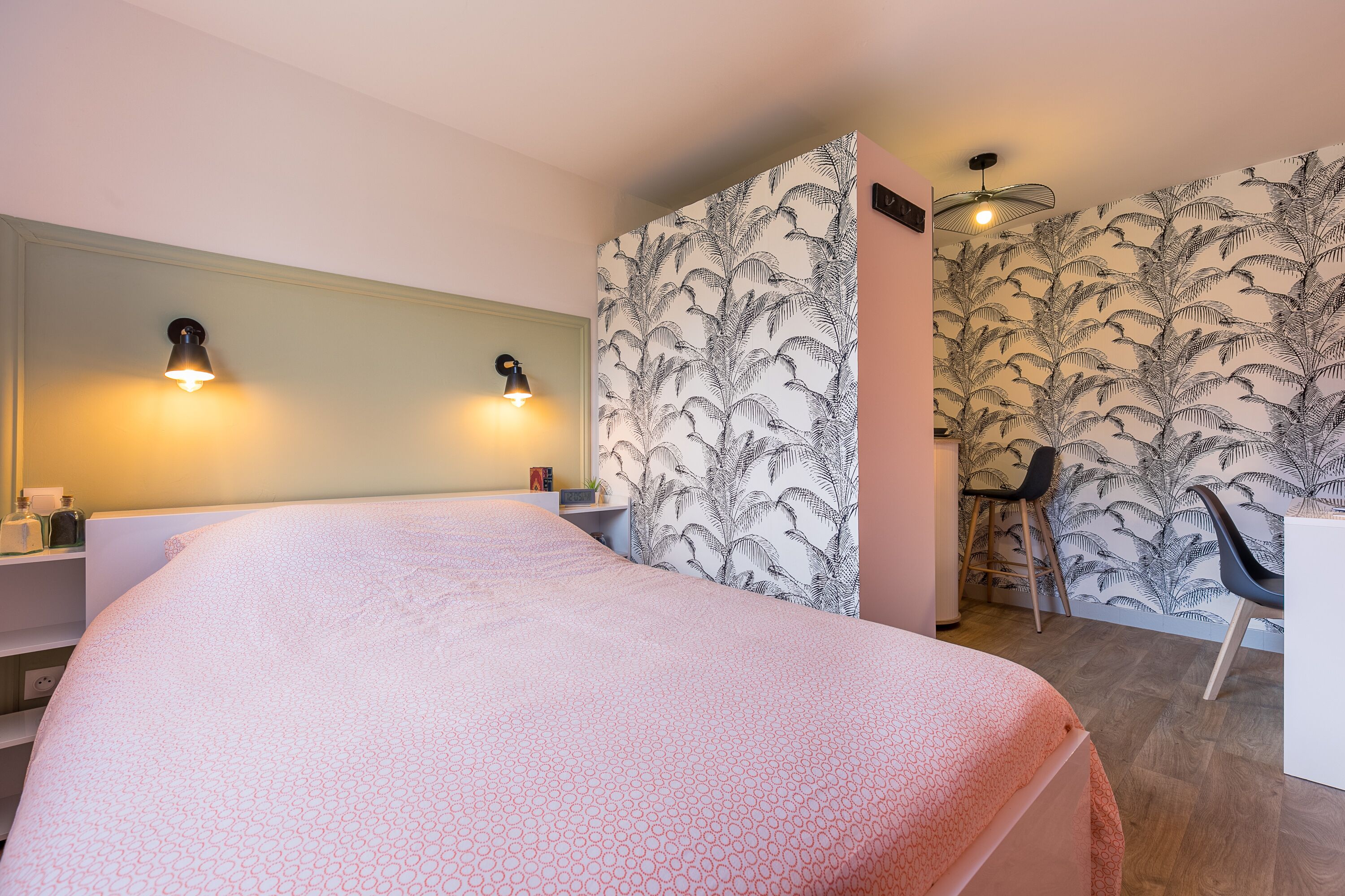 A bedroom with a bed, two wall-mounted lights, a desk, and a chair.