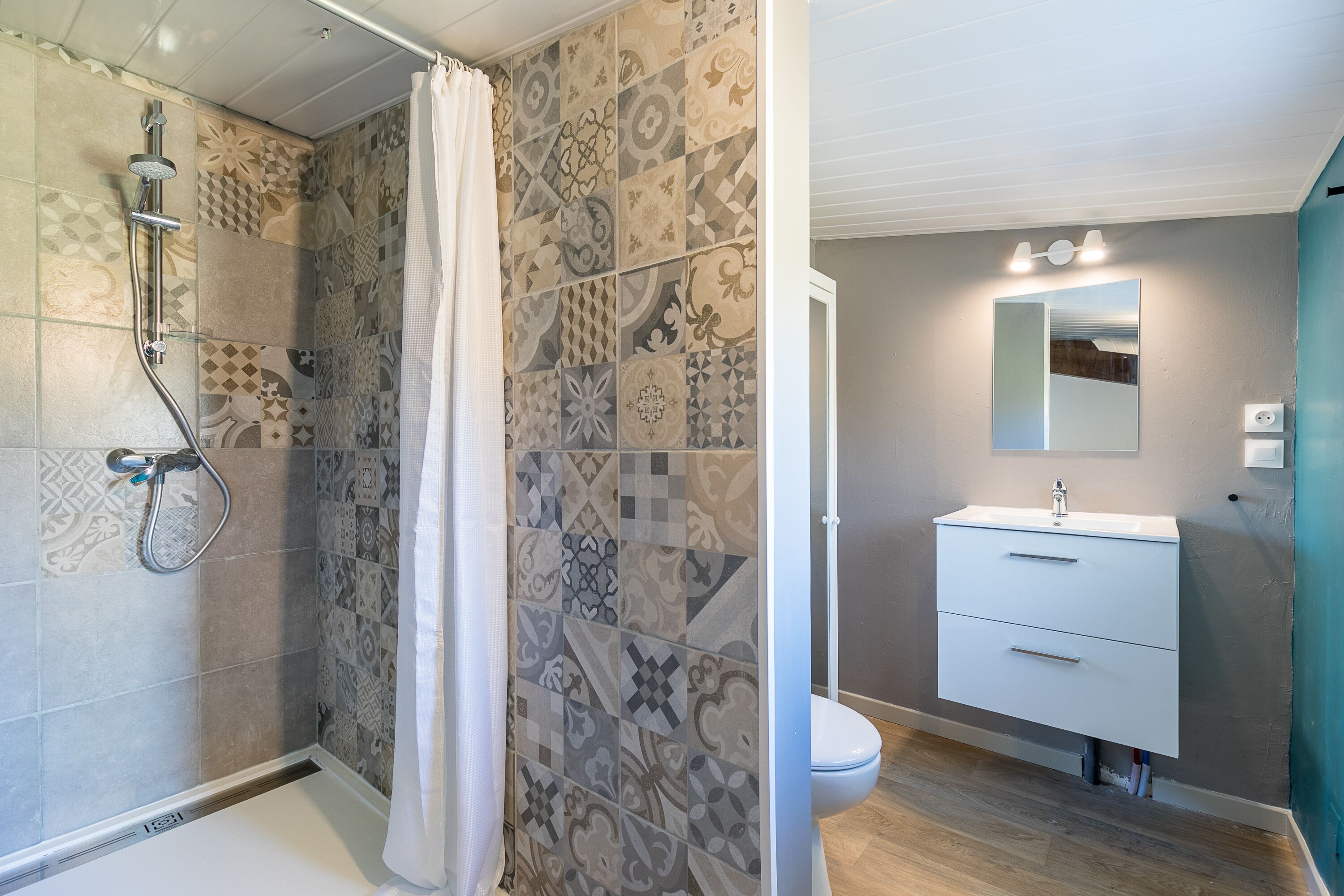 A bathroom with patterned tiles, a shower with a glass door, a white sink, and a mirror above it.