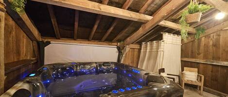 A hot tub with blue LED lights, wooden beams, and hanging plants in a rustic room.