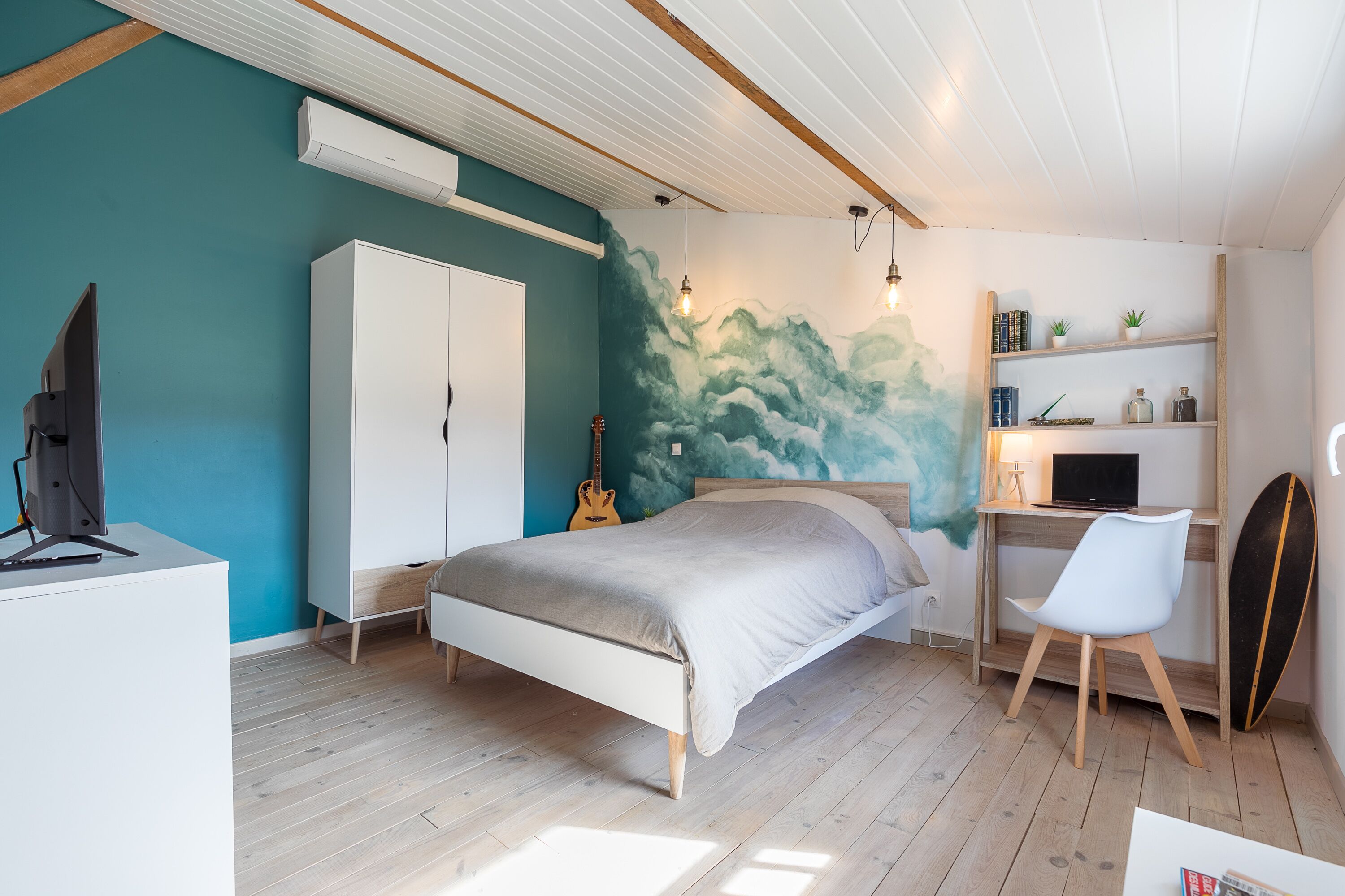 Une chambre avec un lit, un bureau, une guitare et une planche de surf.