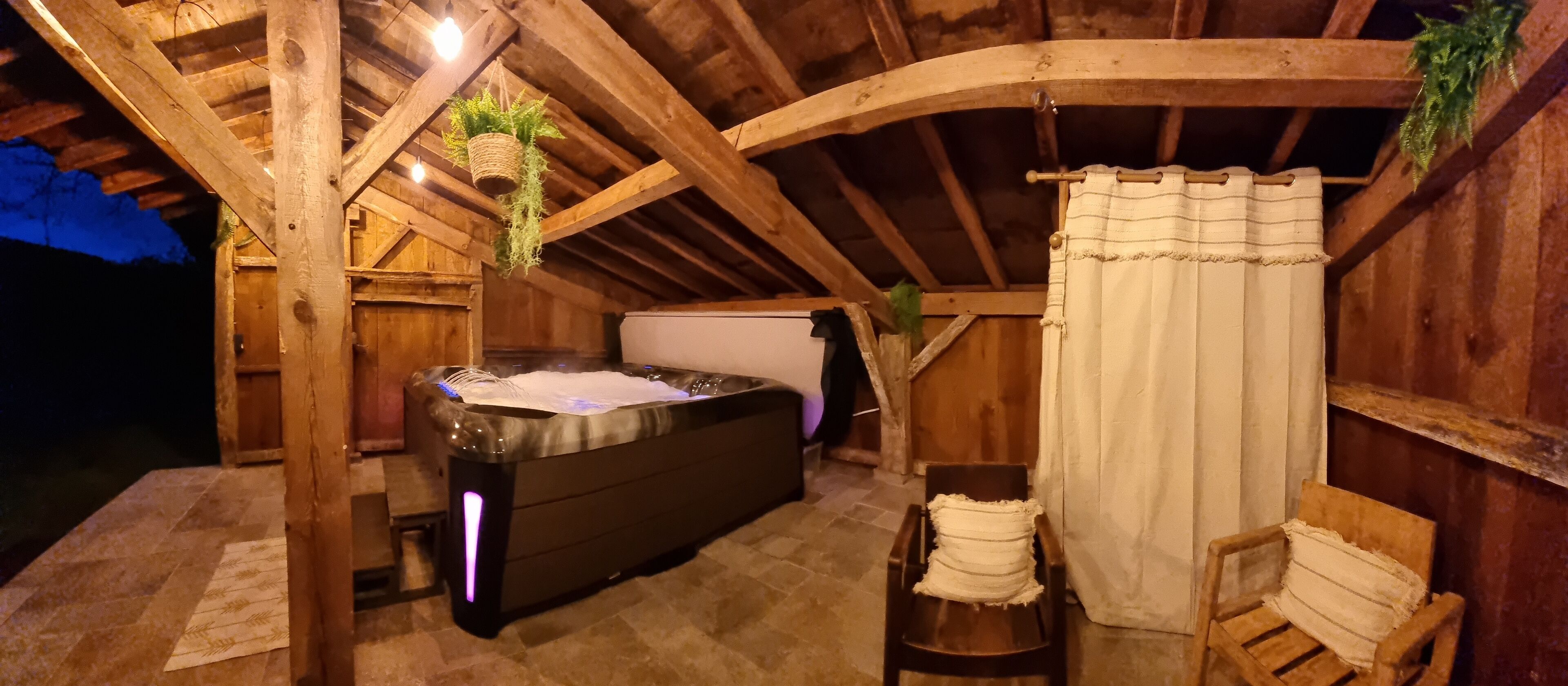 Un bain à remous dans une pièce en bois dotée d’un plafond incliné, d’un rideau et d’une plante suspendue.