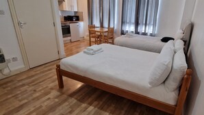 A hotel room with two beds, a wooden floor, a kitchenette, and a dining area. - Urban Retreat Studio Camberwell Zone 2 (London)