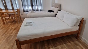 A double bed with a wooden frame and white bedding, a wooden table with chairs, and a window with curtains. - Urban Retreat Studio Camberwell Zone 2 (London)