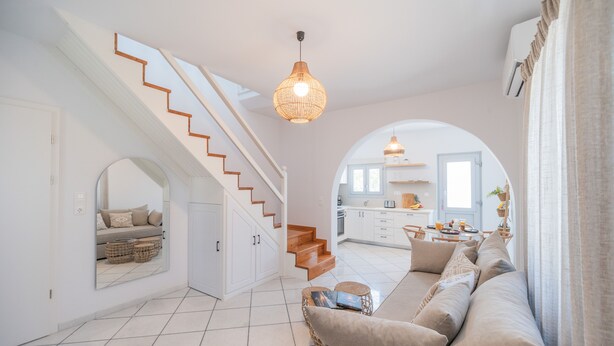 Ein geräumiger Wohnbereich mit Treppe, einem großen Spiegel, einer Couch und einer durch einen Bogen sichtbaren Küche.