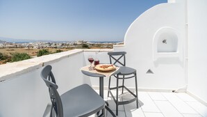Ein Balkon mit zwei Stühlen, einem Tisch, einer Speiseplatte und einem Weinglas.