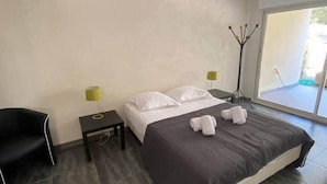 A modern hotel room with a large bed, a black chair, a small table, and a floor lamp. - Appartement T3 - 50M DE LA Plage - Rupione (PIETROSELLA)