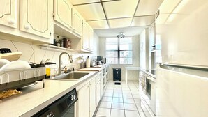 A modern kitchen with white cabinets, a dishwasher, a sink, and a window providing natural light.