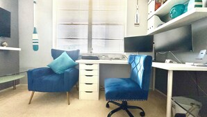 A modern office space with a desk, two chairs, a computer, and a shelf with decorative items.