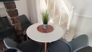 A small dining area with a round table, two chairs, a potted plant, a fireplace, and a staircase.