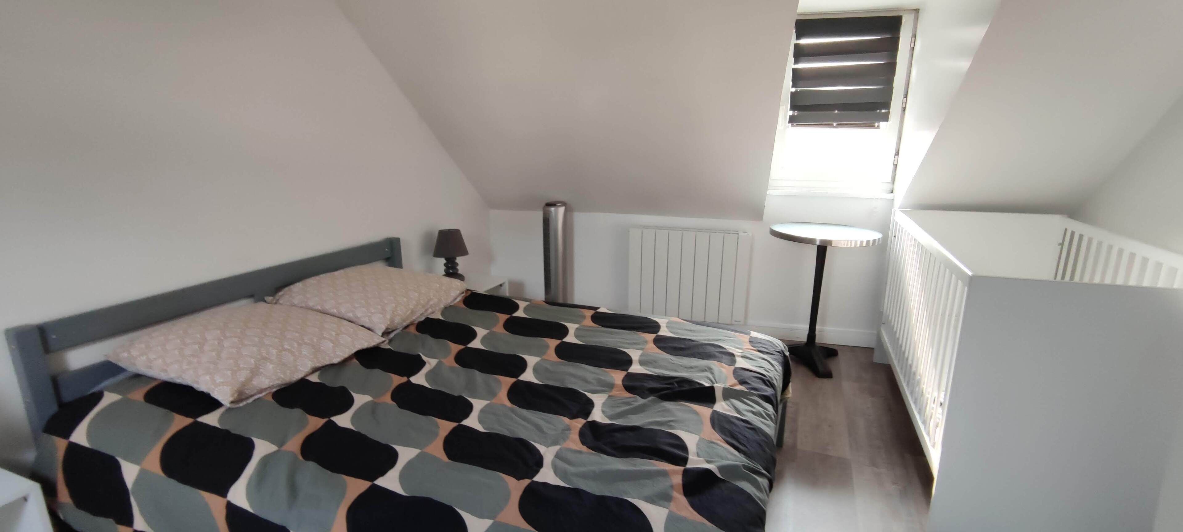 A bedroom with a bed, a bedside table, a lamp, a radiator, and a window with blinds.