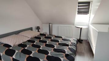 A bedroom with a bed, a bedside table, a lamp, a radiator, and a window with blinds.