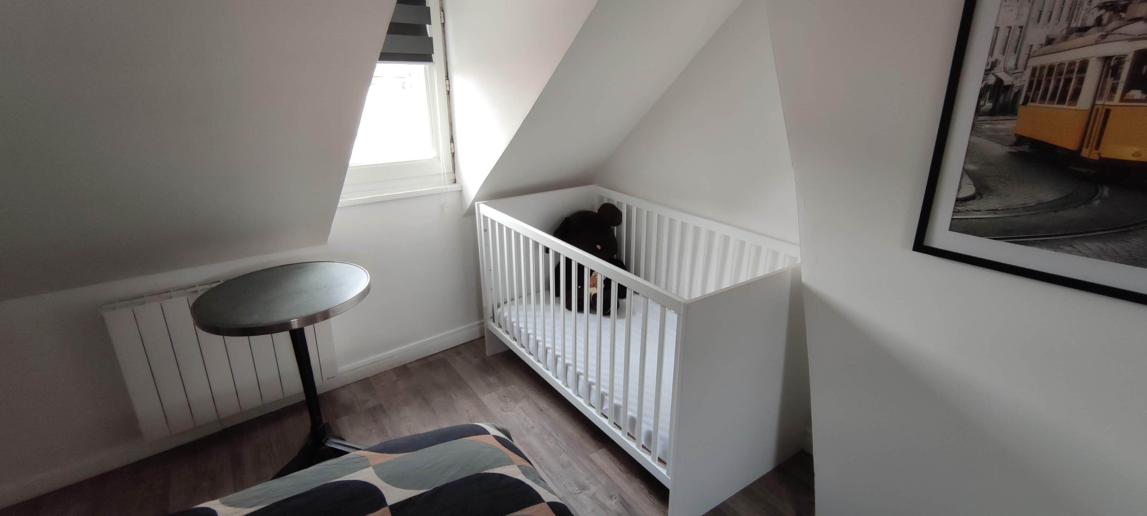 A room with a white crib, a small round table, and a radiator.