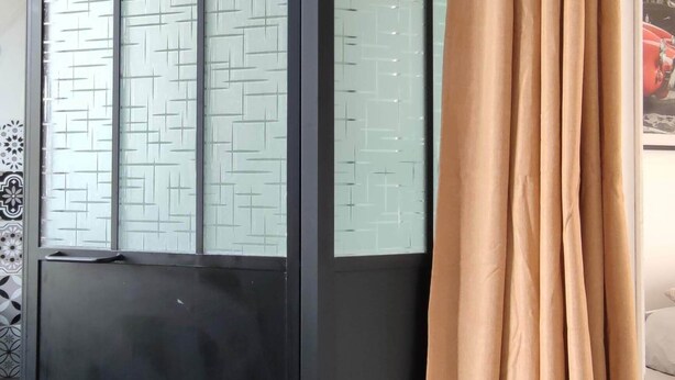 A room with a sliding glass door with a geometric pattern, a beige curtain, and a dark-colored sliding door.