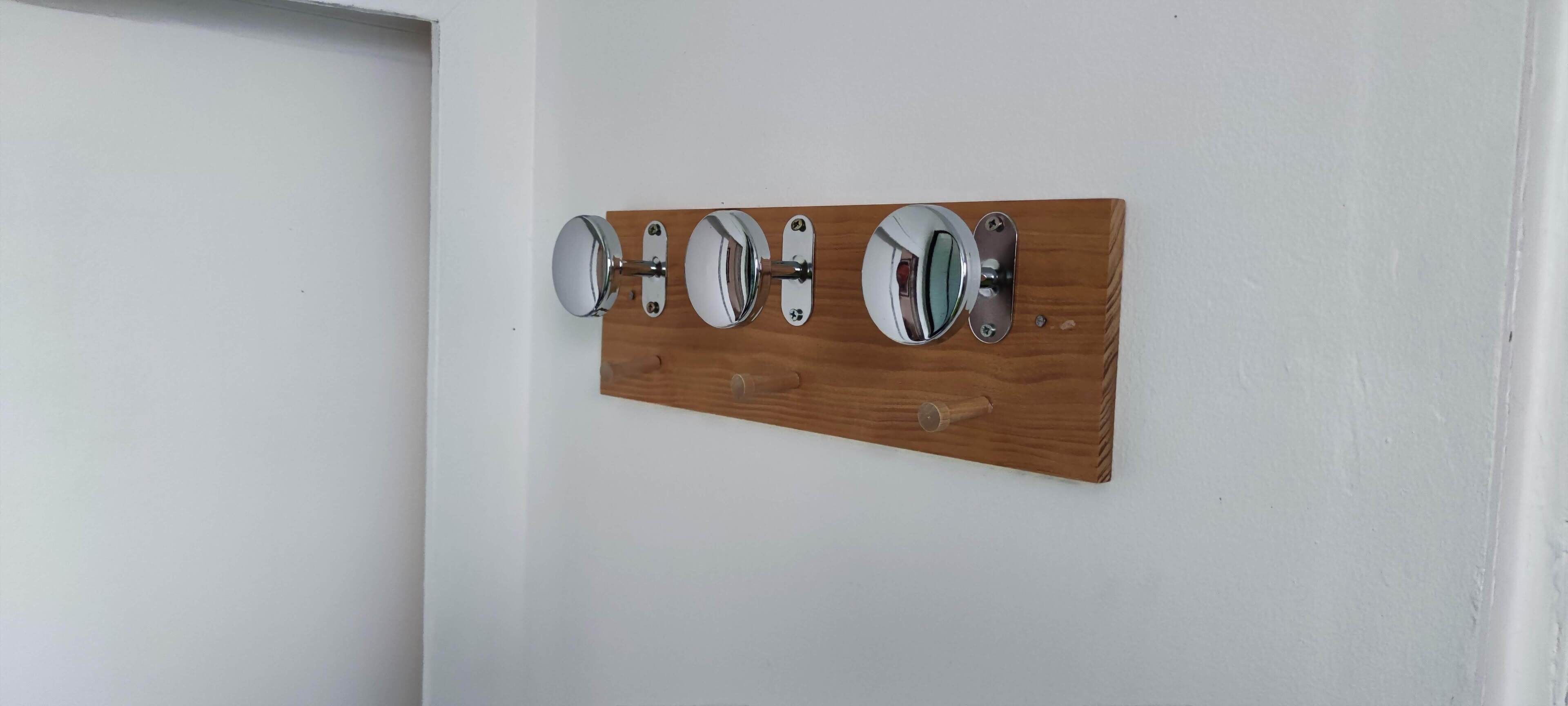 Un pannello di legno fissato alla parete, con tre specchi circolari e una maniglia centrale.