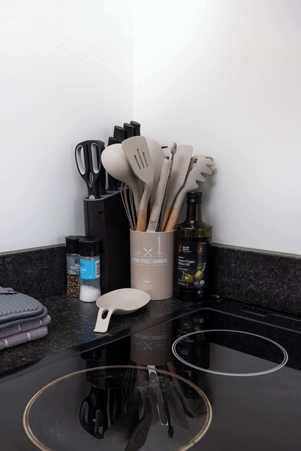 Una encimera de cocina con utensilios, saleros, pimenteros y una botella de aceite de oliva virgen extra.