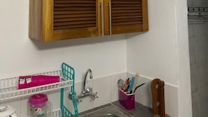 A kitchen with wooden cabinets, a sink, and various kitchen utensils. - Lux Suites Royal Palm Studio Apartment (Mtwapa)