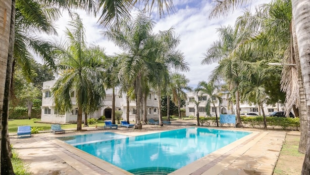A swimming pool surrounded by palm trees and a building with multiple windows. - Lux Suites Royal Palm Studio Apartment (Mtwapa)
