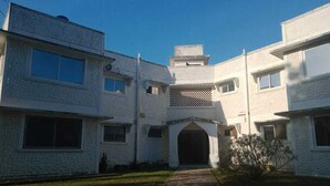 A white building with a central entrance, multiple windows, and a stone pathway leading to the entrance. - Lux Suites Royal Palm Studio Apartment (Mtwapa)