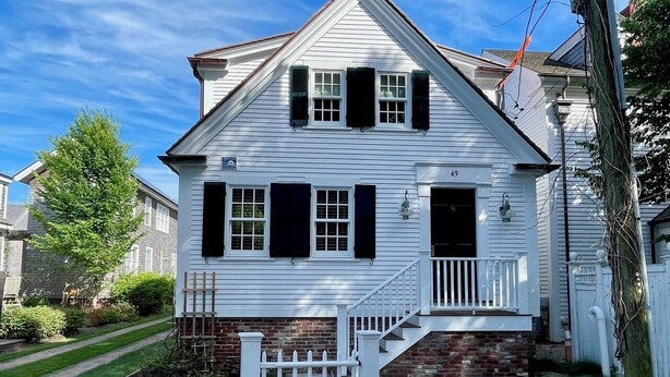 A white two-story house with black shutters, a brick foundation, and a white picket fence. - West End - Commercial Street, Charming 2-Bedroom with Beach Access - Sleeps 4! (Provincetown)