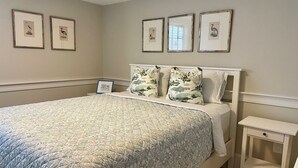 A neatly made bed with a floral-patterned bedspread, a matching pillow, and a bedside table with a drawer. - West End - Commercial Street, Charming 2-Bedroom with Beach Access - Sleeps 4! (Provincetown)