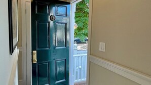 A hallway leading to a dark green door with a small window, a white wall, and a white door frame. - West End - Commercial Street, Charming 2-Bedroom with Beach Access - Sleeps 4! (Provincetown)