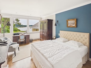 A bedroom with a large bed, a desk, and a view of a lake.