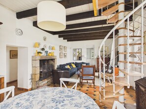 A living room with a fireplace, a blue sofa, a wooden chair, a white spiral staircase, and a clock on the wall.