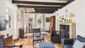 Een woonkamer met een open haard, een houten trap en een eethoek.